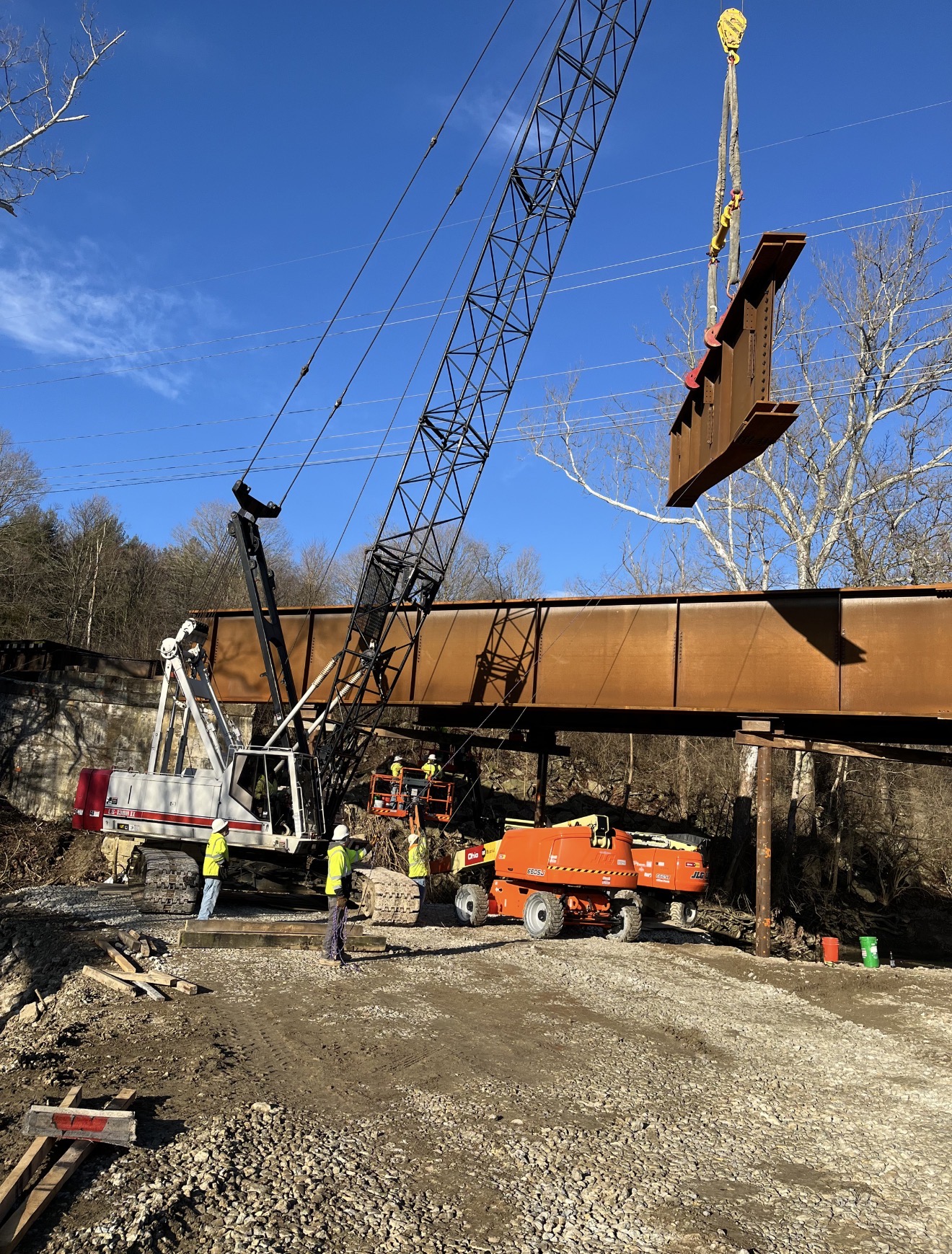 Crane lifting steel girder into place over creek