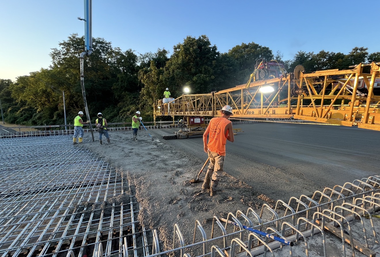 Crew finishing concrete bridge deck at sunset